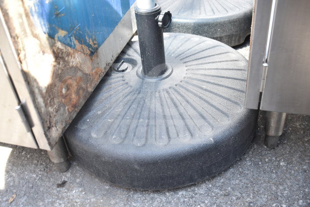 Two durable, black umbrella bases with textured surfaces, shown on a concrete surface, in good condition.