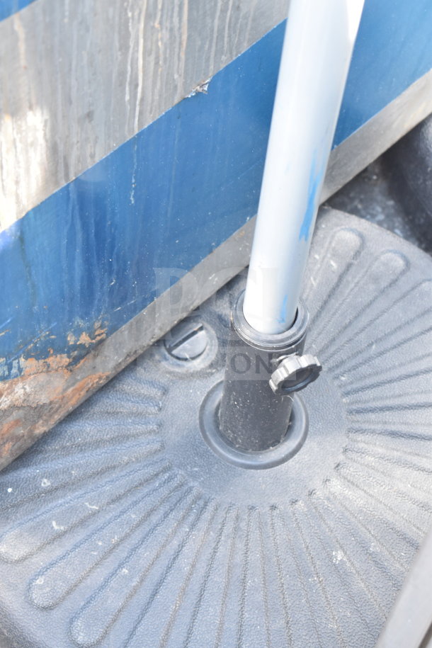 Black umbrella base with textured surface and adjustable knob, holding a metal pole. Slight wear visible.