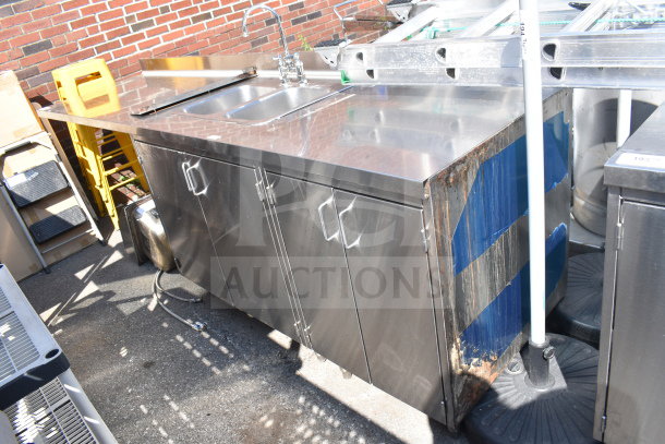 Commercial counter with 2-bay sink and 4 doors, stainless steel, slight rust on the side, outdoor setting. Ideal for heavy use.