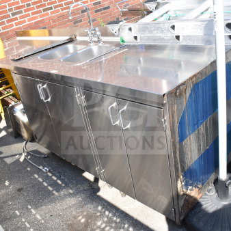 Commercial counter with 2-bay sink and 4 doors, stainless steel, slight rust on the side, outdoor setting. Ideal for heavy use.