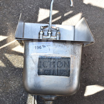 Single bay wall mount sink with faucet, stainless steel, attached hoses, some surface wear, label with auction details visible.