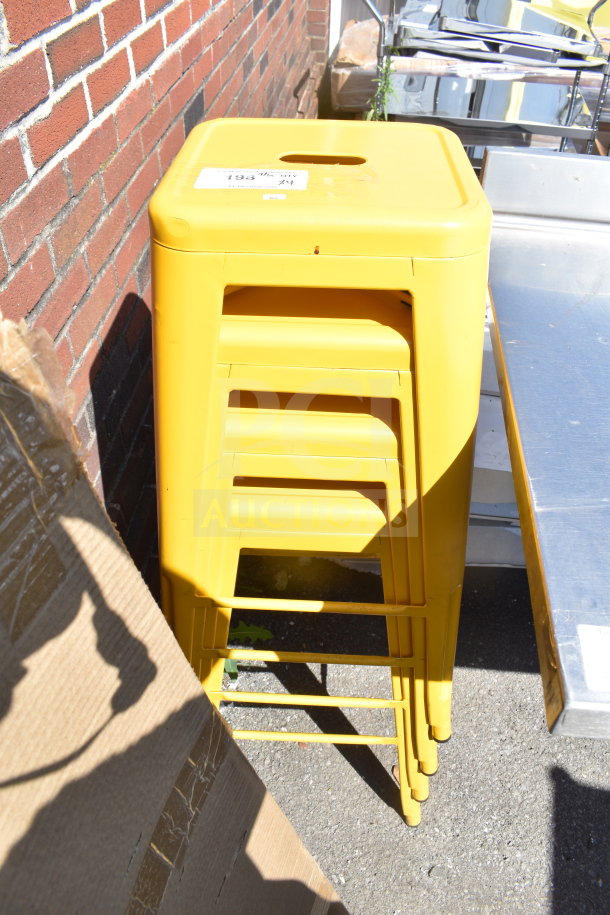 Four yellow Tolix style stools stacked, in good condition, with a visible auction label on the top stool.
