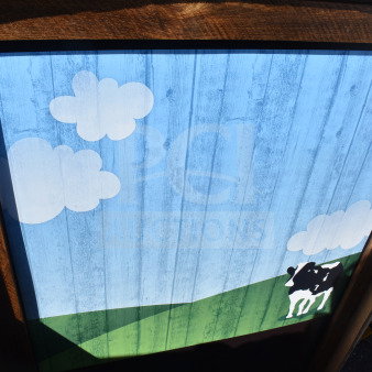Tabletop with cow painting features a whimsical design of a cow, clouds, and field on a blue sky background. Wood frame, vibrant colors.