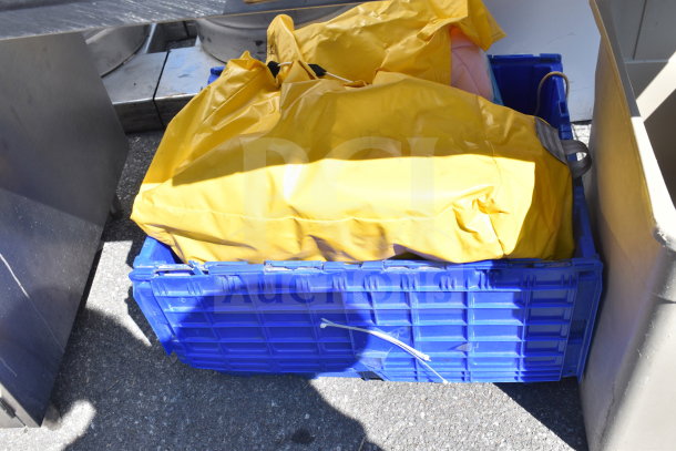 Blue crate containing yellow bag and various items, including a costume and Slim Jim trash can, visible in outdoor setting.