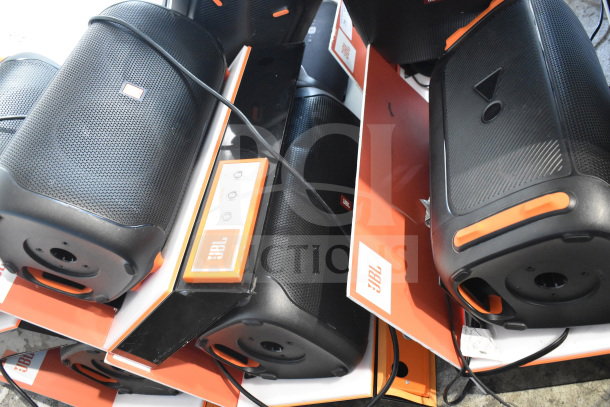 3 JBL speakers on display, featuring sleek black design with orange accents. Includes power controls. Brand labels visible.