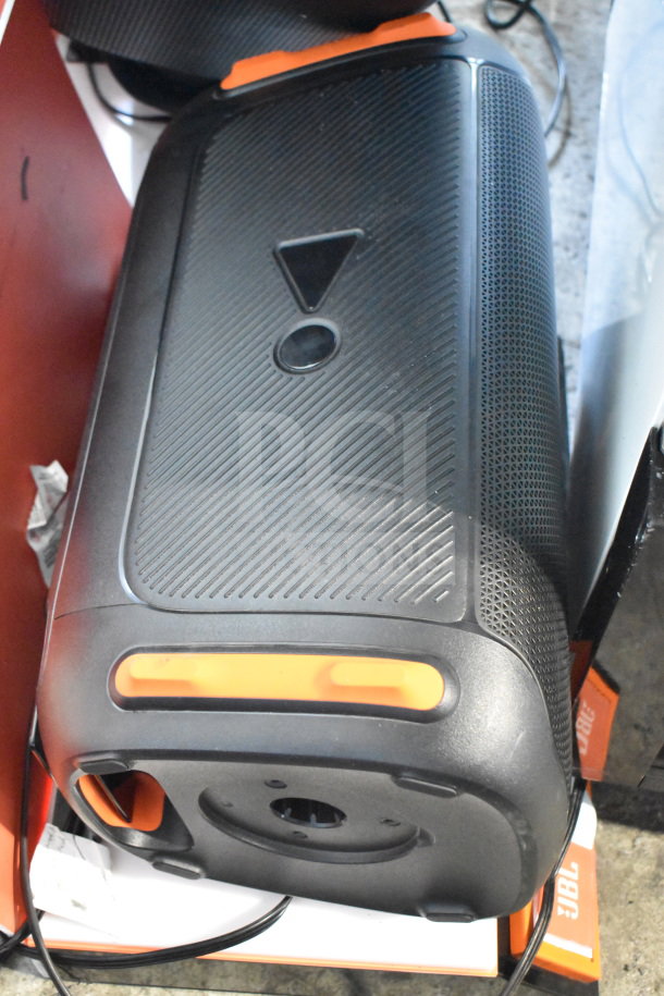 JBL speaker in store display, black with orange accents, featuring a textured exterior and power cable, on shelves.