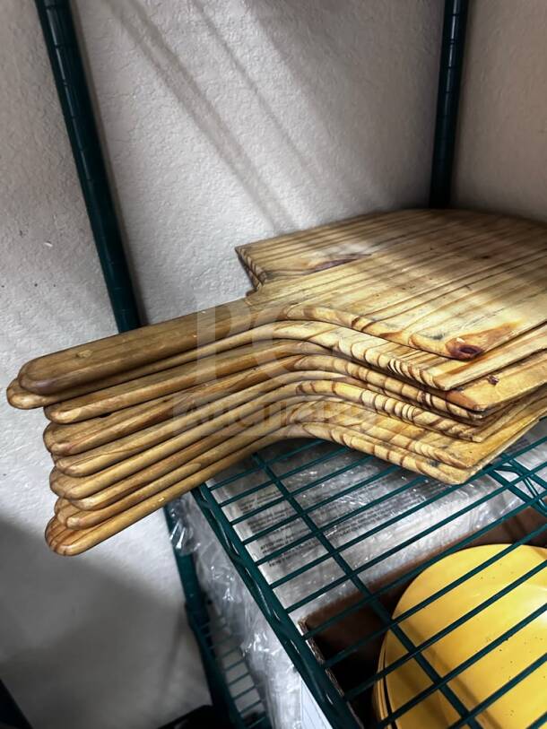 Nine wooden commercial pizza peels by Commercial Kitchen Smallwares, well-maintained, stacked on a shelf.