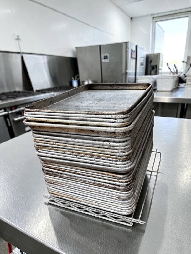 Stack of 30 Commercial Kitchen Smallwares 1/2 Size Aluminum Sheet Pans in used condition, ideal for commercial baking.