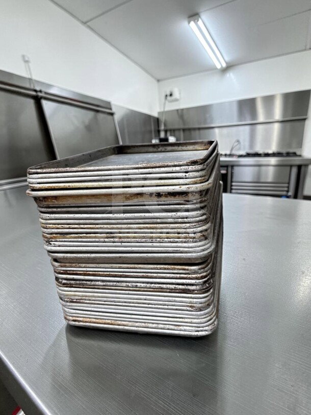 Stack of 30 aluminum half-size sheet pans, Commercial Kitchen Smallwares model, used condition, ideal for commercial use.