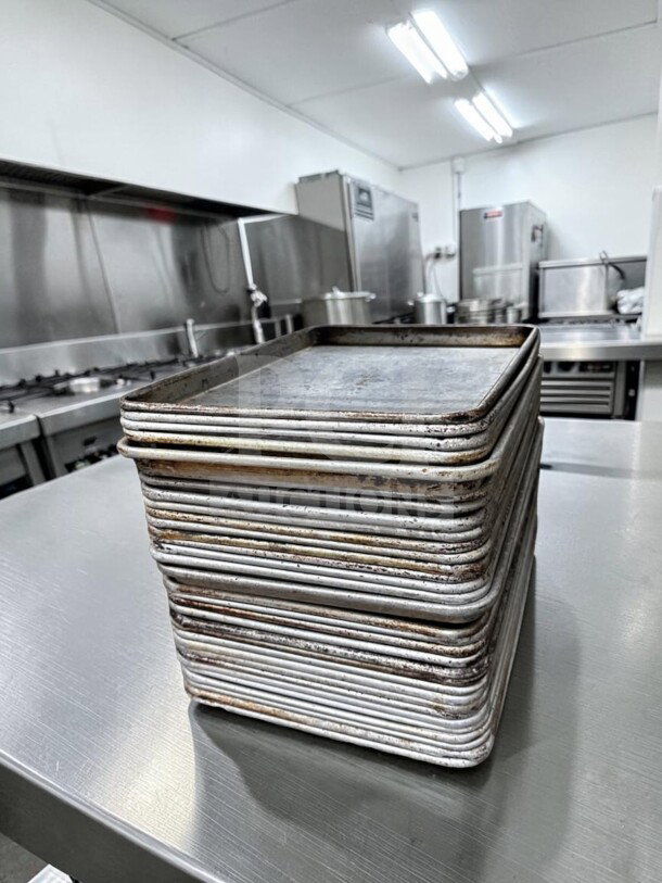 Stack of 30 Commercial Kitchen Smallwares aluminum 1/2 size sheet pans, showing wear, ready for commercial use.