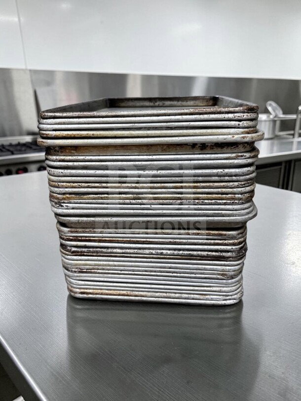 Stack of 30 Commercial Kitchen Smallwares 1/2 Size Aluminum Sheet Pans, showing signs of use, ideal for commercial baking.