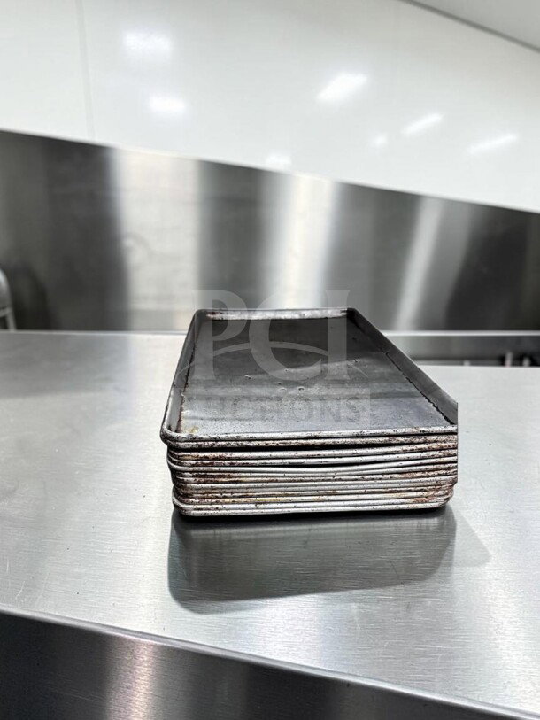 Stack of 13 full-size aluminum sheet pans, well-maintained, from Commercial Kitchen Smallwares, ready for use.