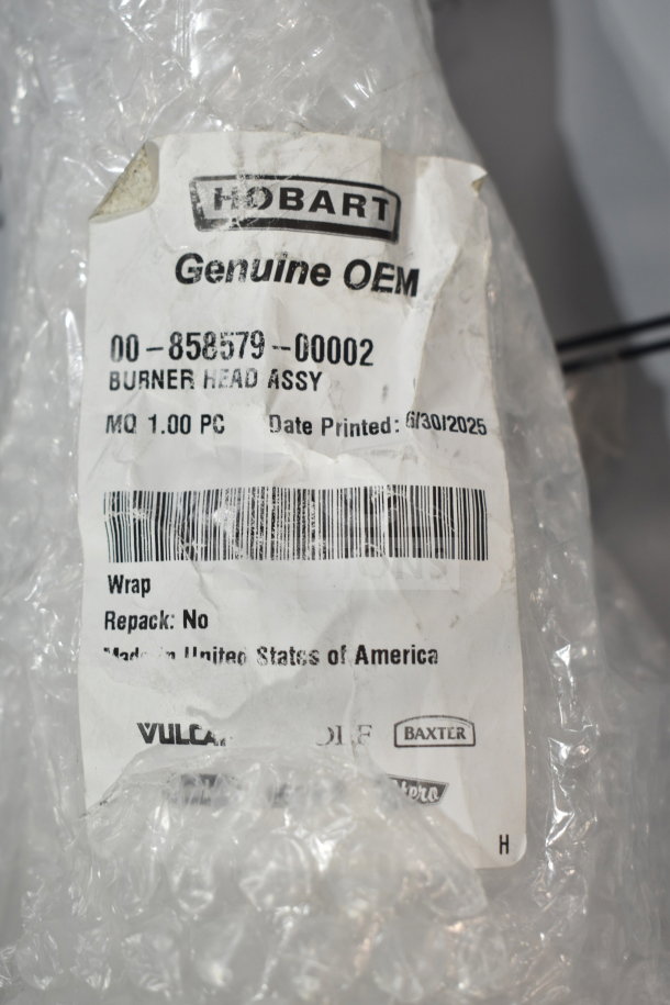 "Brand new Vulcan 00-858579-00002 burner head assembly in bubble wrap. Hobart OEM label with barcode and manufacturing details."