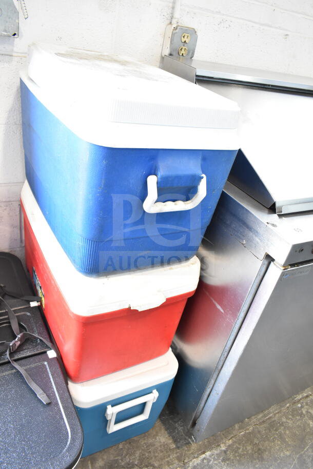 Three portable coolers, two blue and one red, stacked. Used condition. Ideal for outings and picnics.
