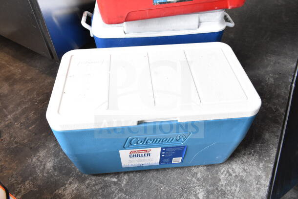 Three portable coolers; two blue Coleman Chillers and one red cooler. Visible brand label, sturdy construction.