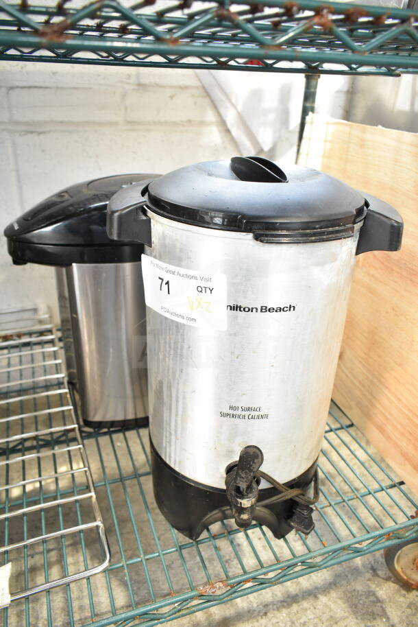Hamilton Beach beverage dispenser and Eurolux dispenser on metal shelf; both feature black lids and silver bodies.