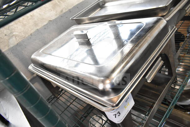 4 stainless steel chafing dishes, rectangular with lids, in good condition, stacked on a metal rack; auction label visible.