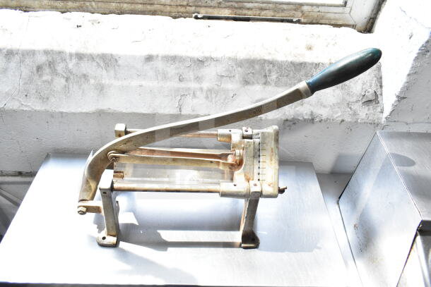 Countertop French fry cutter with metal frame and black handle, showing wear. Brand Vollrath visible on handle.