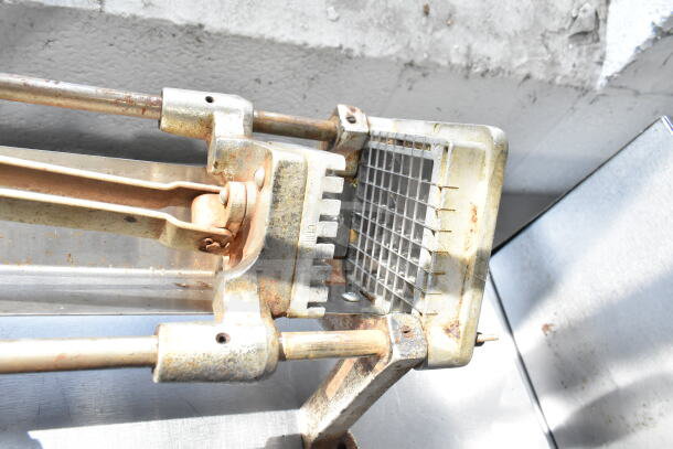 Rusty countertop French fry cutter with metal grid and handle, showing signs of wear. Marked with "China."