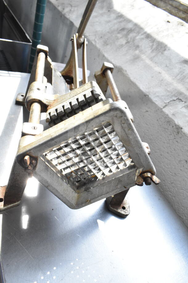 Countertop French fry cutter with metal frame and grid blade, showing signs of rust and wear, suitable for kitchen use.