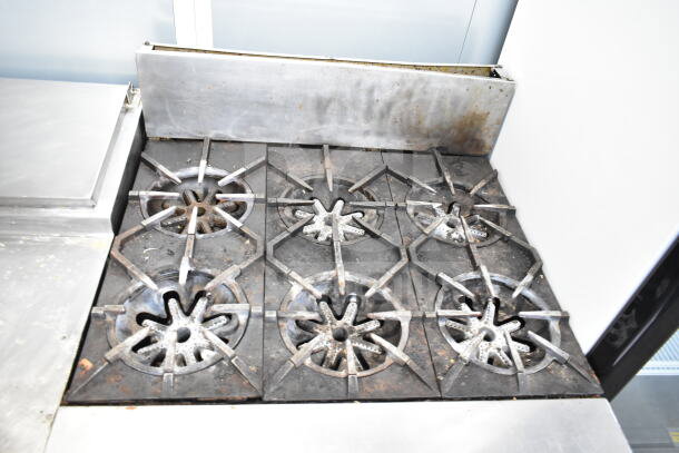 Garland commercial gas-powered 6 burner range with convection oven, showing signs of use. Sturdy metal construction.