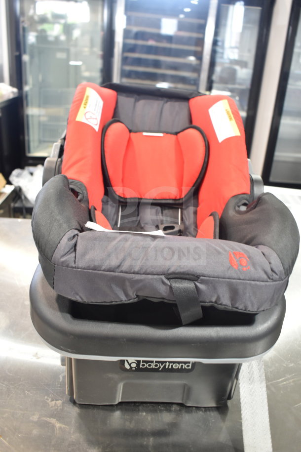 Babytrend Infant Car Seat with Base, red and black, gently used condition, safety labels visible, secure and cushioned.