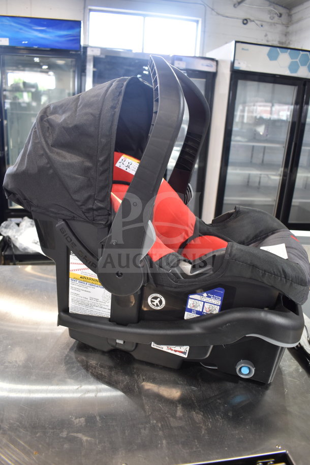 Babytrend infant car seat with base, black and red, side-impact protection, adjustable handle, and warning labels visible.