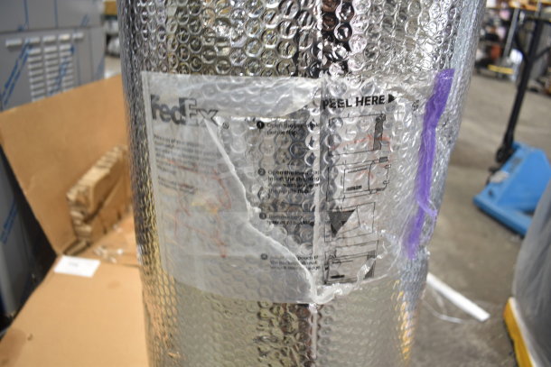 Roll of bubble wrap packaging with FedEx label, visible peel instructions, in warehouse setting.