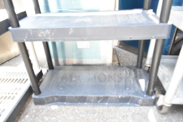 Black poly 4-tier shelving unit, sturdy construction, moderate wear, ideal for storage, no visible labels or markings.