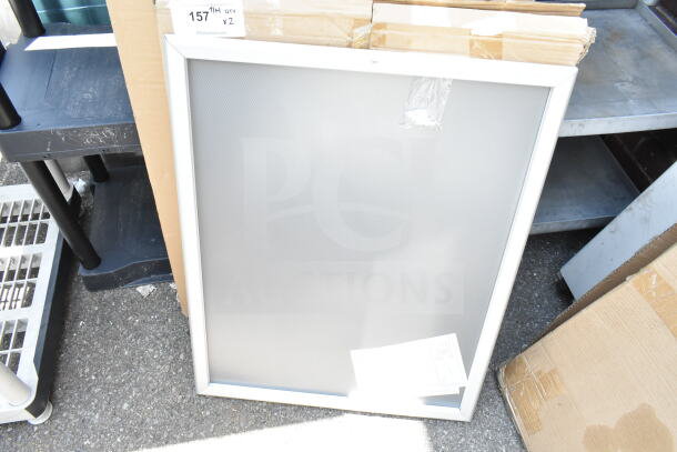 Two units of white-framed panels, pristine condition, leaning against a cardboard box; auction lot tag visible.