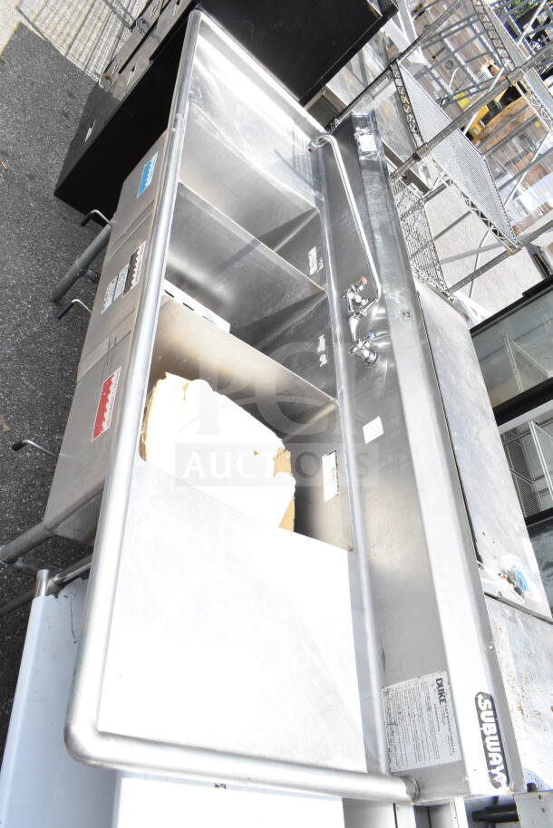 Stainless steel Duke commercial 3-bay sink with dual drain boards. Includes faucet and handles. Subway and Duke labels visible.