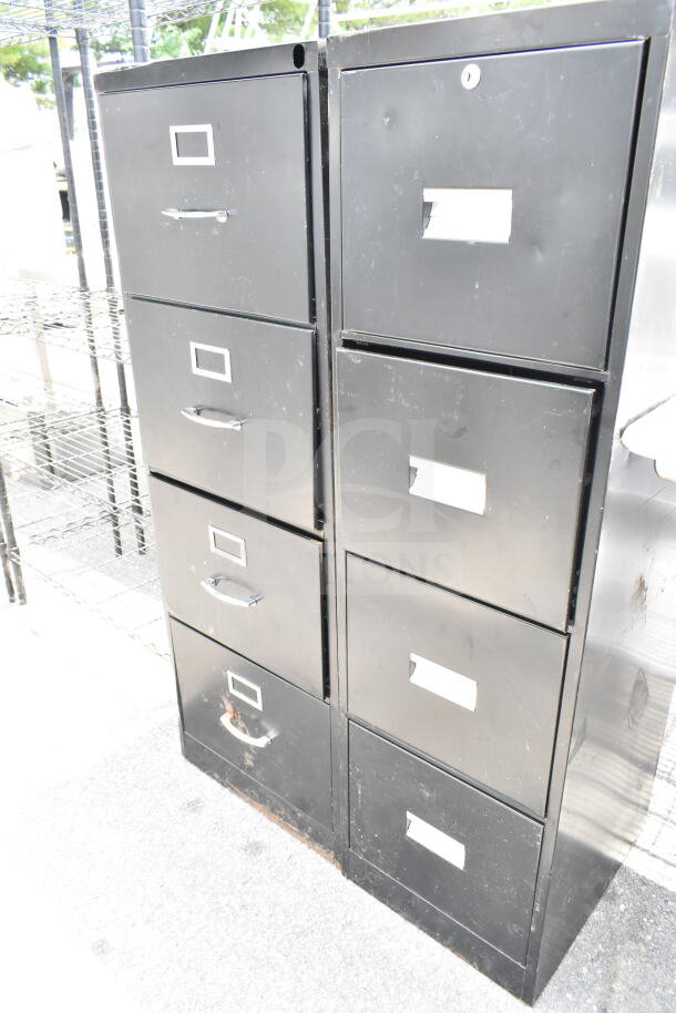 Two black 4-drawer filing cabinets with label holders and handles. Visible wear and marks. Suitable for office storage.