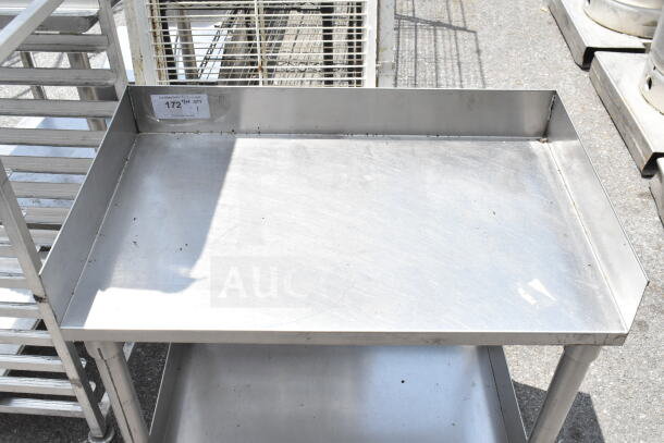 Stainless steel commercial equipment stand with under shelf on casters, in used condition. Includes a visible label indicating "172."