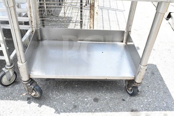 Commercial equipment stand with under shelf on sturdy casters, stainless steel, signs of use, suitable for industrial settings.