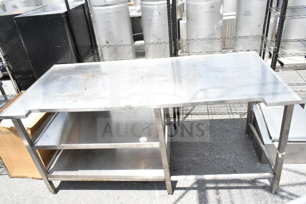 Commercial stainless steel table with two under shelves, showing moderate wear. Ideal for industrial kitchen use.