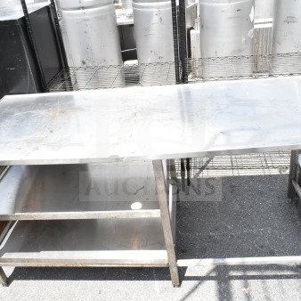 Commercial stainless steel table with two under shelves, showing moderate wear. Ideal for industrial kitchen use.