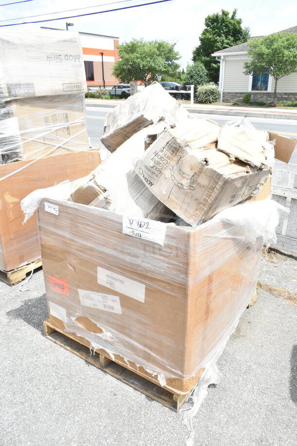 Cardboard boxes of scratch and dent items, including compressor and hotel pans, on a wooden pallet wrapped in plastic.