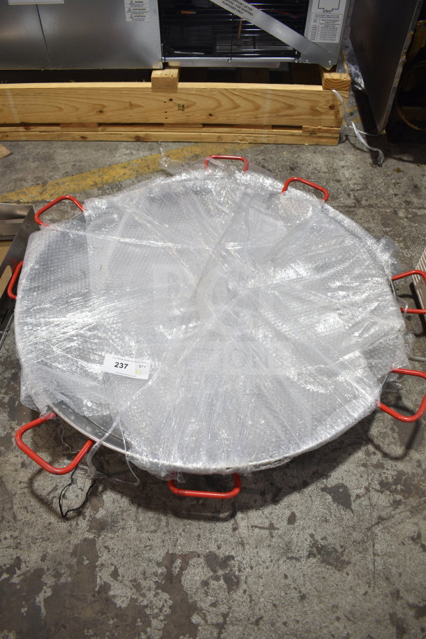 New polished carbon steel paella pan with red handles, wrapped in plastic, labeled "237 QTY XL." Scratch and dent condition.