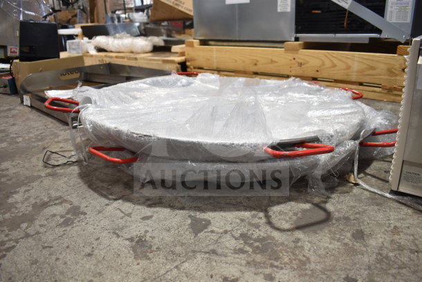 Two brand new polished carbon steel paella pans, wrapped in plastic, visible red handles, slight scratch and dent.