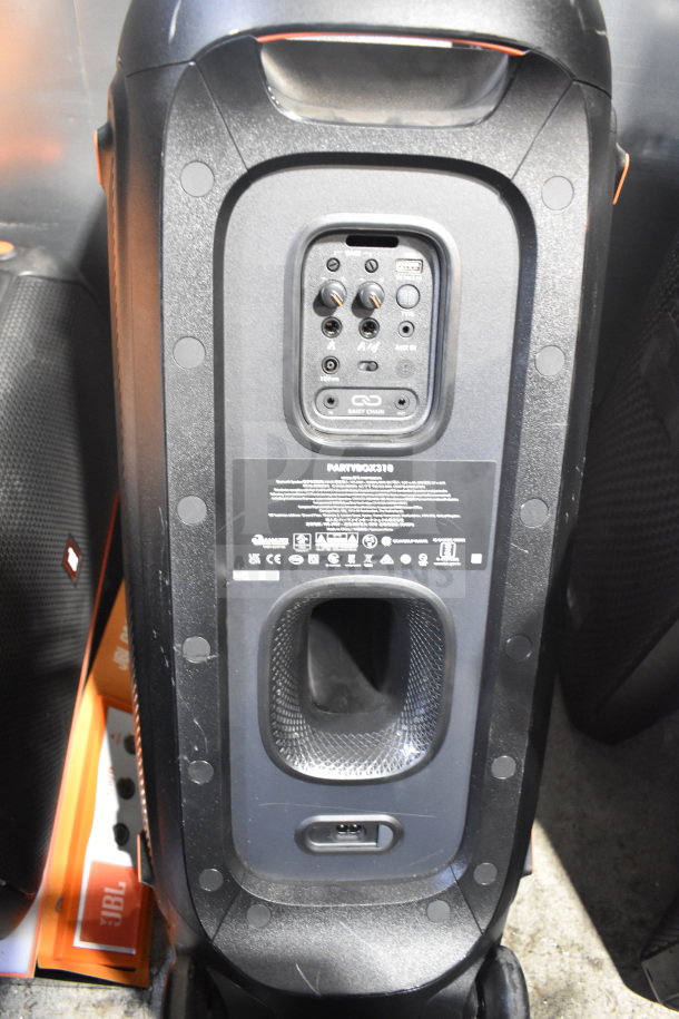 JBL Partybox 310 speaker, black, with control panel and various input ports. Features labels and daisy chain function.