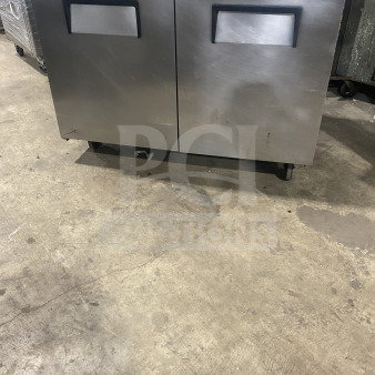 Two-door stainless steel undercounter refrigerator or freezer, commercial, maintained condition, with handles and wheels.