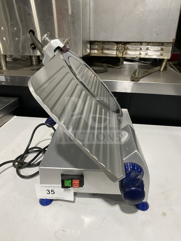 Commercial stainless-steel electric countertop meat slicer, on legs, features power switches, numbered dial, and visible cord.