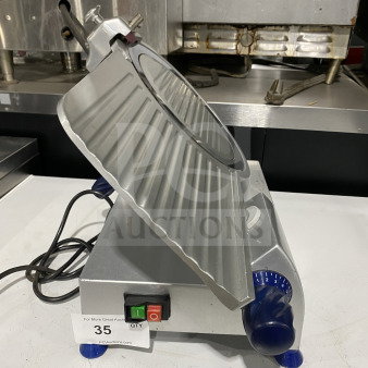 Commercial stainless-steel electric countertop meat slicer, on legs, features power switches, numbered dial, and visible cord.
