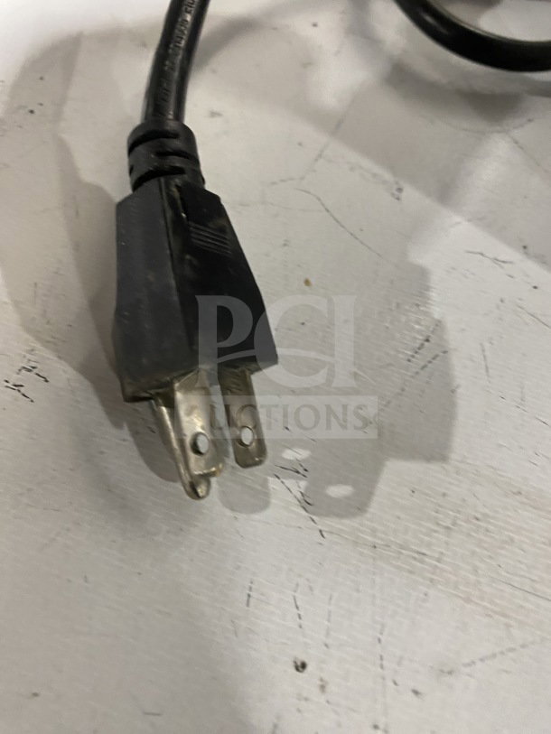A close-up of the power plug for a commercial stainless-steel electric meat slicer. Plug shows wear.