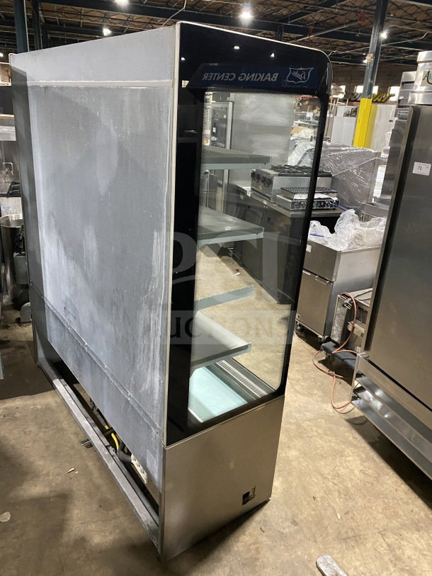 Commercial stainless-steel open-air merchandiser, electric powered, three shelves, used condition, visible "Baking Center" label.