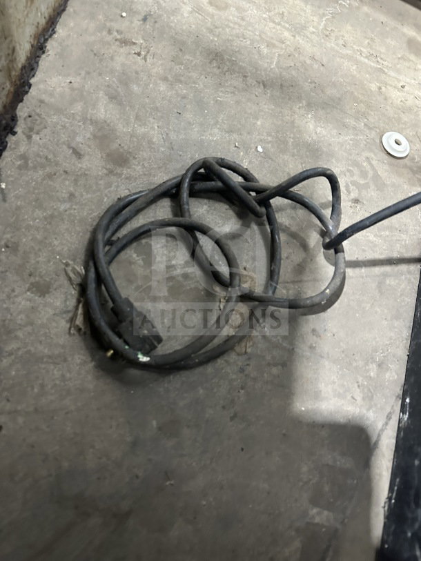 Coiled black power cord on concrete floor, detached from Habco ESM12 refrigerator. Cord appears worn but intact.
