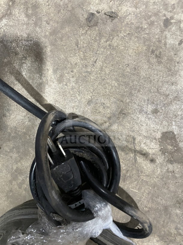 Coiled black electrical cord for a commercial refrigerated bakery/deli display case, showing a standard plug.