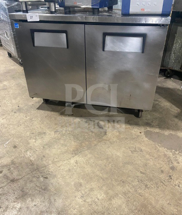 Two-door stainless steel undercounter refrigerator or freezer, commercial, maintained condition, with handles and wheels.