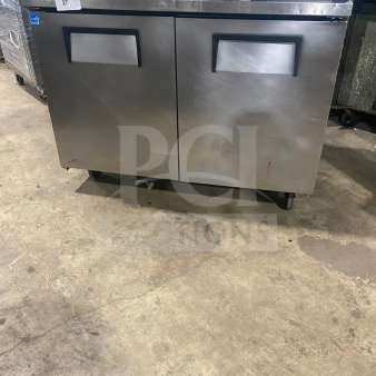 Two-door stainless steel undercounter refrigerator or freezer, commercial, maintained condition, with handles and wheels.