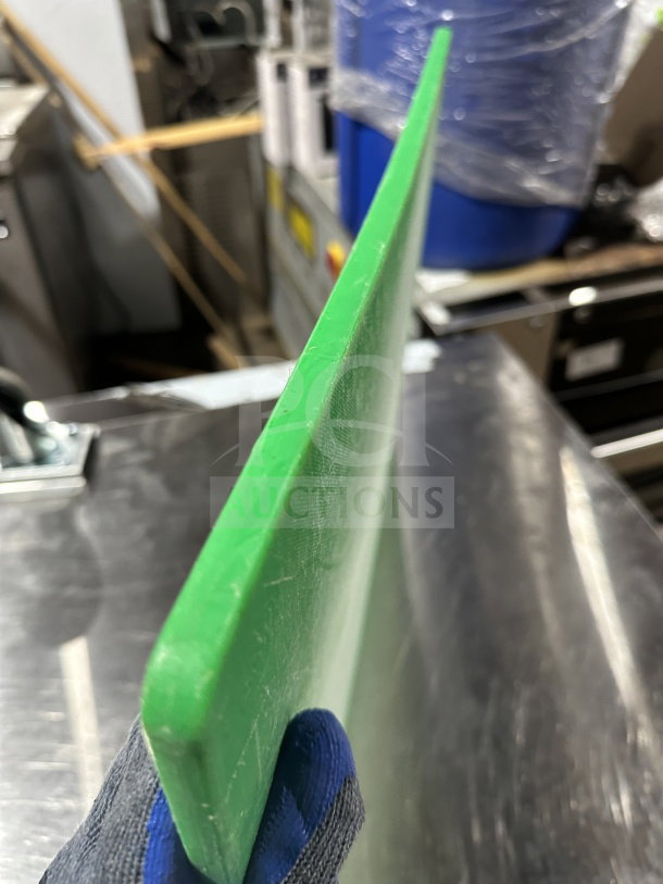 Green commercial plastic cutting board, used condition, durable and non-porous surface, visible wear.